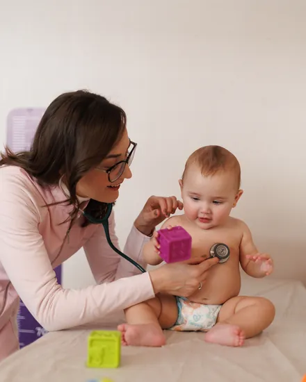 Dra. Ana Bürger examinando um bebê com o estetoscópio no consultório